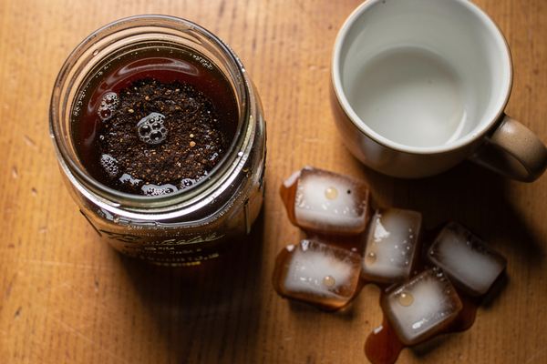 A glass jar of cold brew coffee steeping with coffee grounds on a kitchen counter