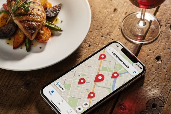 A phone showing a restaurant map search next to a plate of food on a wooden table